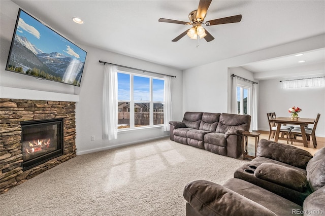 living room with carpet floors, a wealth of natural light, a stone fireplace, and baseboards