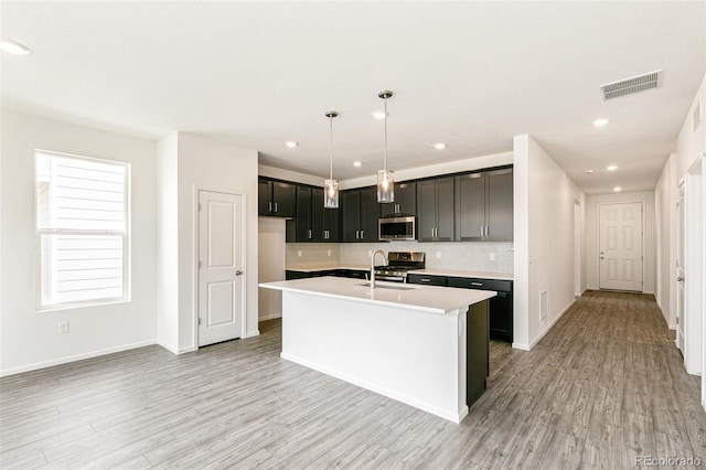 13322 E 110th Way, Commerce City, CO 80022 - kitchen featuring appliances with stainless steel finishes, light countertops, a kitchen island with sink, tasteful backsplash, and light wood-style floors