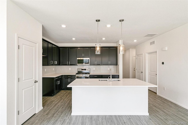 13322 E 110th Way, Commerce City, CO 80022 - kitchen with stainless steel appliances, decorative backsplash, an island with sink, light wood-style flooring, and recessed lighting