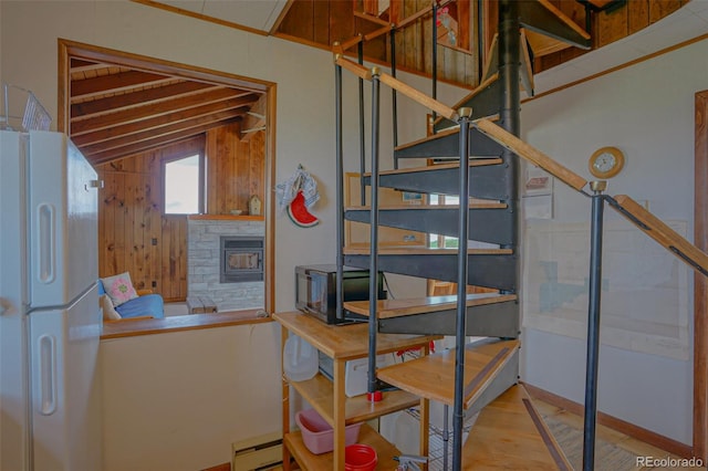 stairway featuring a baseboard heating unit, hardwood / wood-style flooring, lofted ceiling, wooden walls, and a stone fireplace