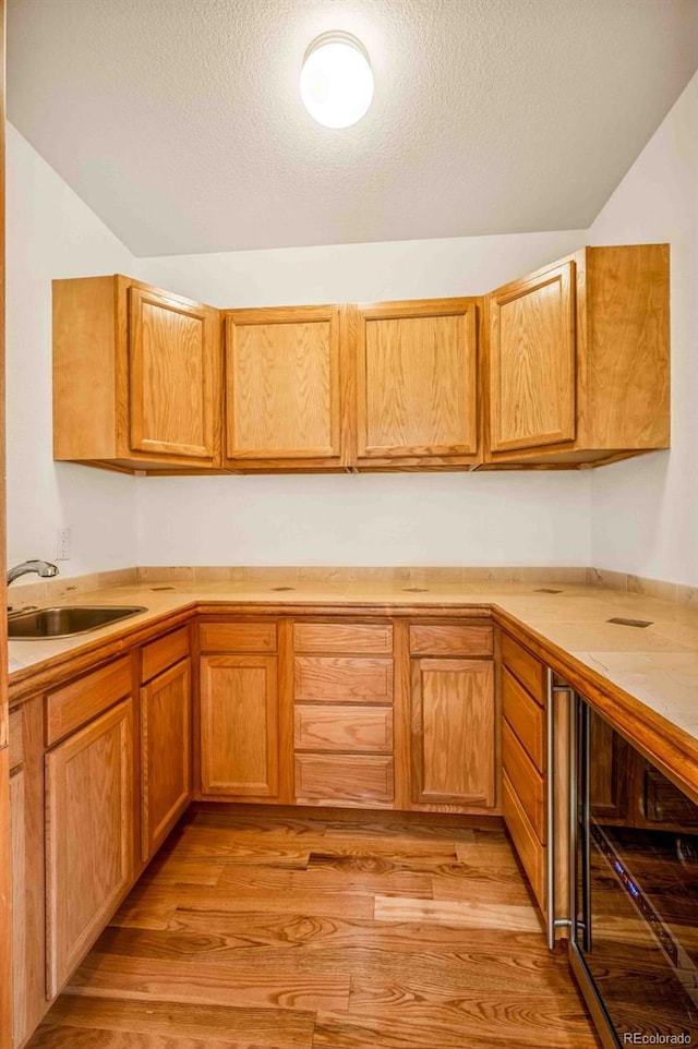 7506 Urban Ct, Arvada, CO 80005 - kitchen featuring wine cooler, light countertops, light wood-style flooring, a textured ceiling, and brown cabinets