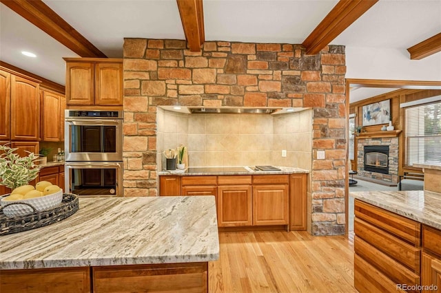7506 Urban Ct, Arvada, CO 80005 - kitchen with stainless steel double oven, light stone countertops, beam ceiling, light wood-style floors, and tasteful backsplash