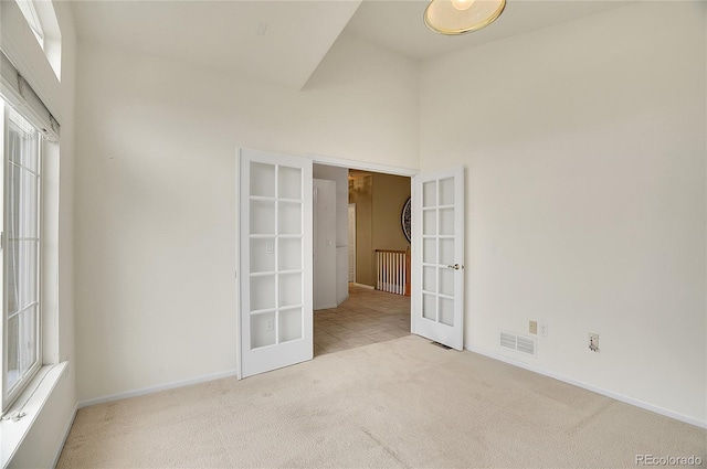 empty room with carpet flooring, a towering ceiling, visible vents, baseboards, and french doors