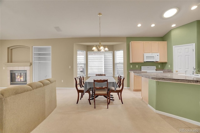 dining room with a tiled fireplace, light colored carpet, lofted ceiling, a chandelier, and recessed lighting