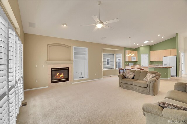 living room with light carpet, baseboards, a tile fireplace, lofted ceiling, and ceiling fan with notable chandelier