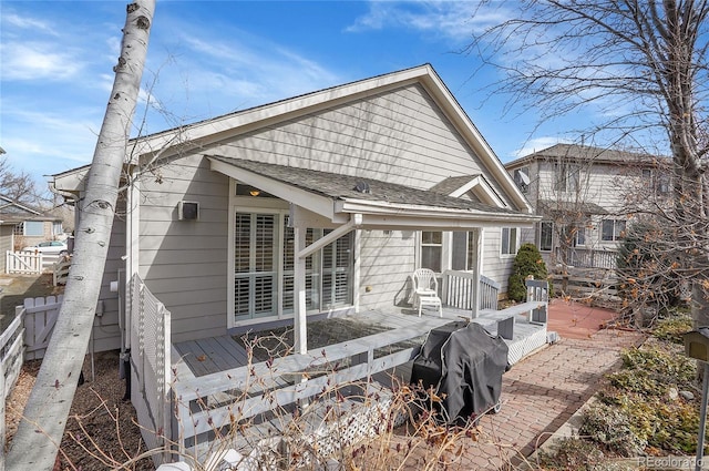 back of house with roof with shingles, fence, and a wooden deck