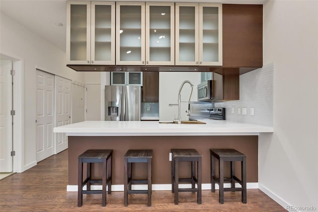 kitchen with a kitchen bar, decorative backsplash, dark wood-type flooring, and stainless steel appliances