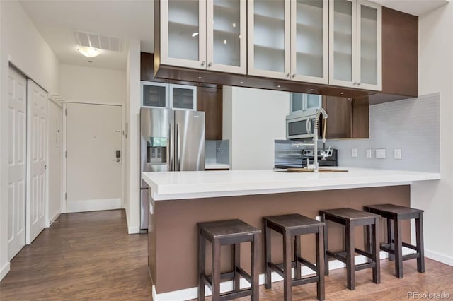 kitchen featuring kitchen peninsula, backsplash, dark hardwood / wood-style floors, stainless steel appliances, and a kitchen bar