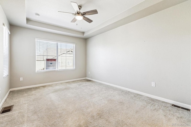 carpeted empty room with ceiling fan and a raised ceiling