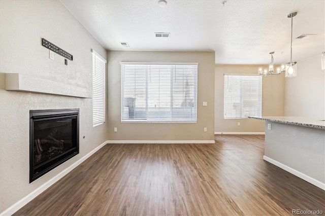 unfurnished living room featuring dark wood-type flooring, a textured ceiling, and a chandelier