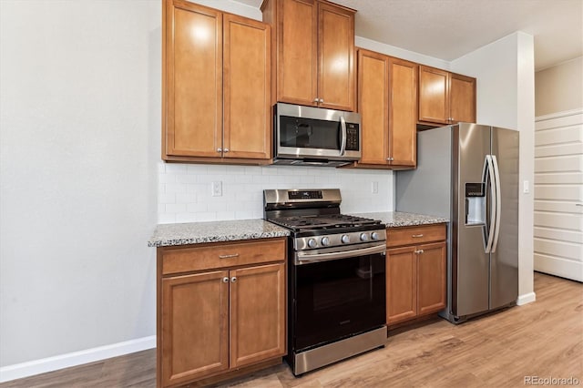 kitchen with light stone countertops, appliances with stainless steel finishes, light hardwood / wood-style flooring, and tasteful backsplash