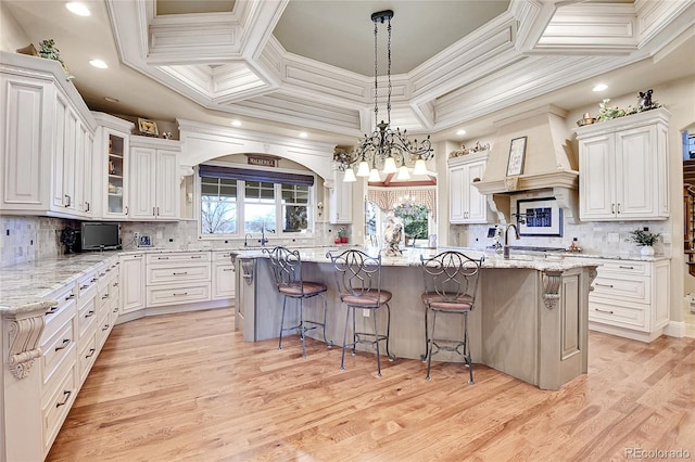 kitchen with a notable chandelier, white cabinets, a breakfast bar, and an island with sink