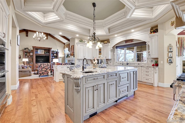 kitchen with pendant lighting, sink, white cabinetry, an island with sink, and light stone counters