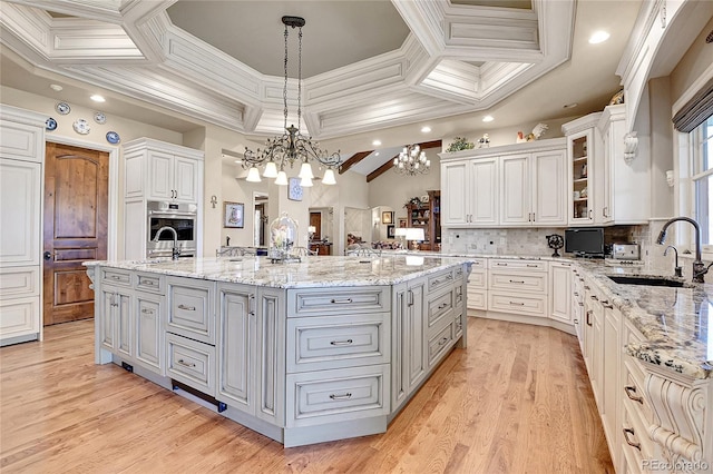 kitchen featuring gray cabinets, an island with sink, decorative backsplash, a notable chandelier, and white cabinets