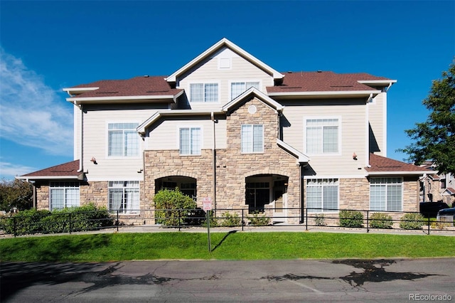 view of front facade with a shingled roof, stone siding, and fence