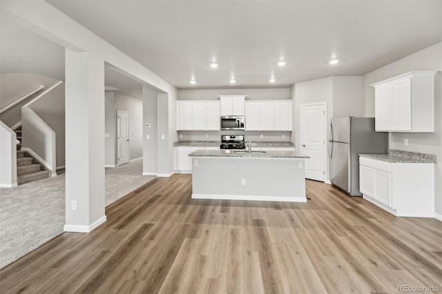 2175 Alyssa St, Fort Lupton, CO 80621 - kitchen featuring stainless steel appliances, light wood-type flooring, white cabinetry, baseboards, and an island with sink