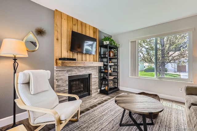 living area featuring baseboards, wood finished floors, and a stone fireplace