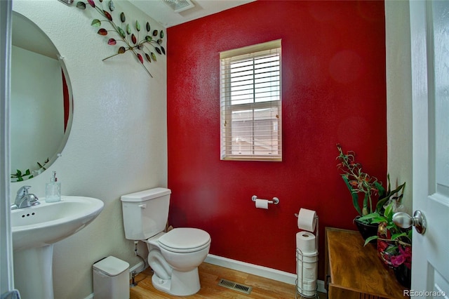 half bath with toilet, baseboards, visible vents, and wood finished floors