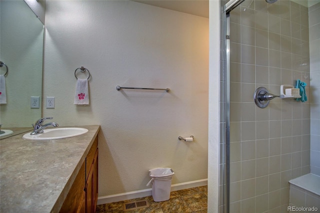 bathroom featuring visible vents, a tile shower, vanity, and baseboards