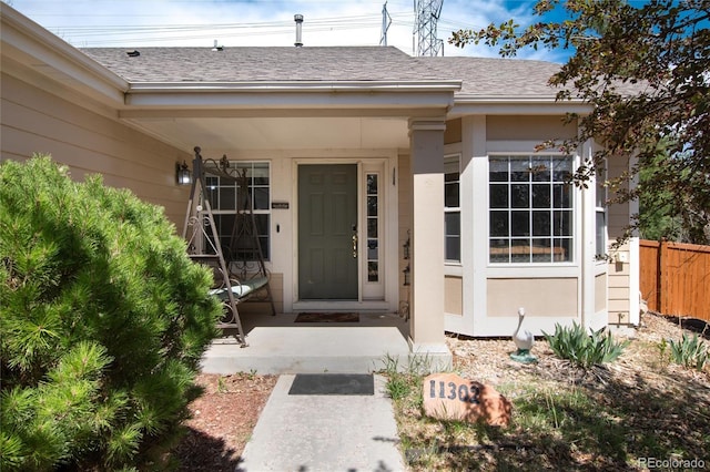 property entrance featuring roof with shingles and fence
