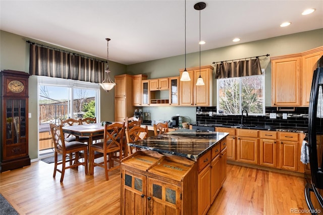 kitchen featuring a sink, light wood-style floors, a center island, glass insert cabinets, and tasteful backsplash