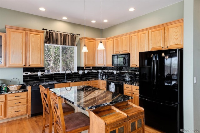 kitchen featuring black appliances, a sink, light brown cabinets, tasteful backsplash, and a kitchen breakfast bar