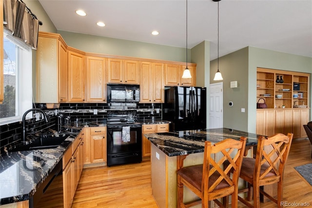 kitchen featuring black appliances, a sink, backsplash, light wood-style floors, and a breakfast bar