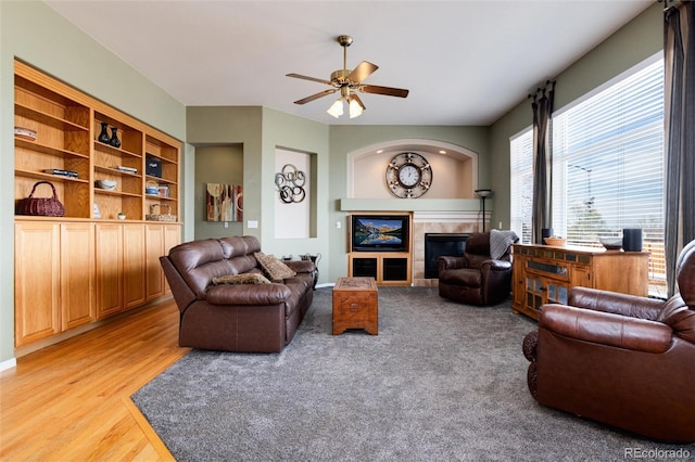 living area with a ceiling fan, a fireplace, and light wood-type flooring