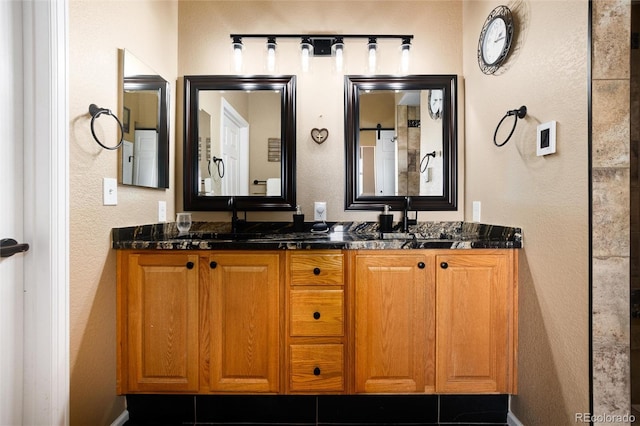 bathroom with a textured wall, double vanity, and baseboards