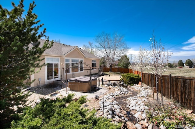 rear view of house with a hot tub, a fenced backyard, and a patio