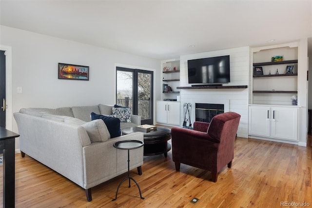 living room with a large fireplace, built in features, and light wood-type flooring