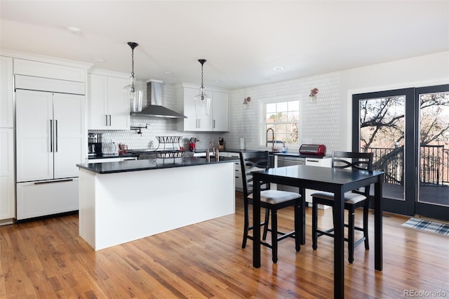 kitchen featuring white cabinets, paneled fridge, a kitchen island, and wall chimney range hood