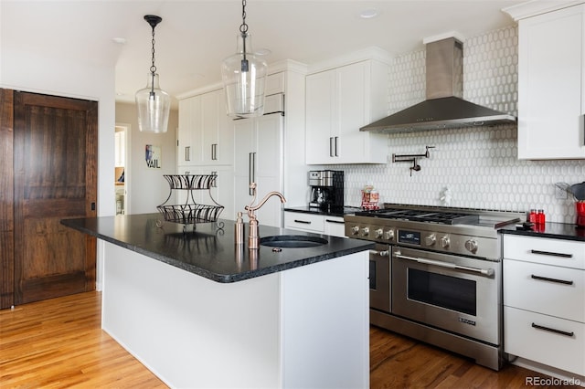 kitchen with sink, premium appliances, white cabinets, a center island with sink, and wall chimney exhaust hood