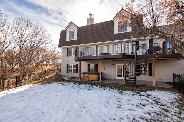 snow covered rear of property featuring a hot tub and a deck