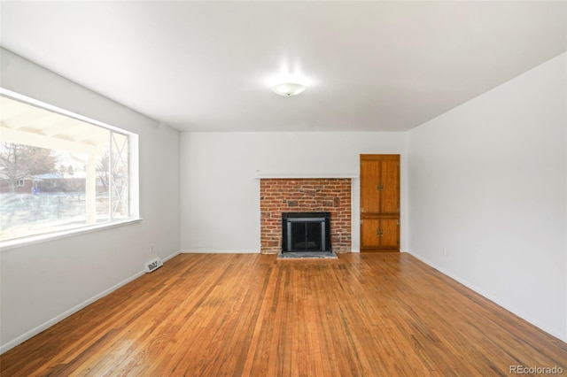 unfurnished living room featuring hardwood / wood-style flooring and a brick fireplace