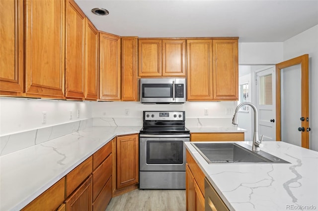 kitchen with light hardwood / wood-style floors, light stone countertops, sink, and appliances with stainless steel finishes