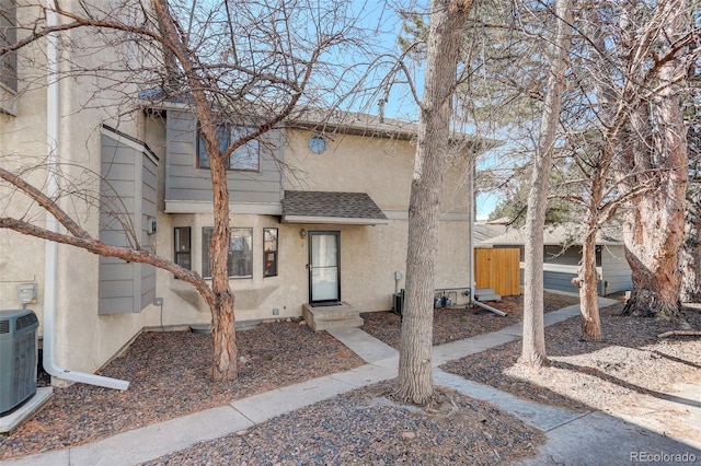 view of front of home with stucco siding, central AC, and roof with shingles