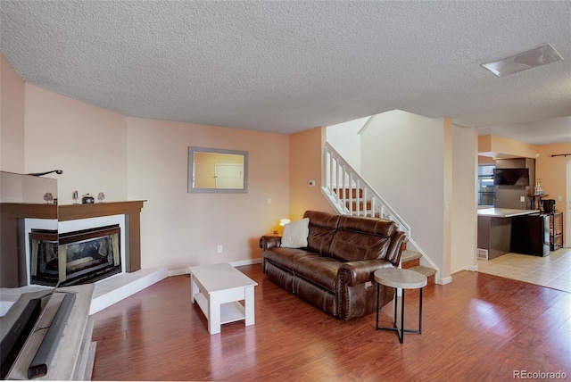 living area with stairway, baseboards, light wood-style floors, and a glass covered fireplace