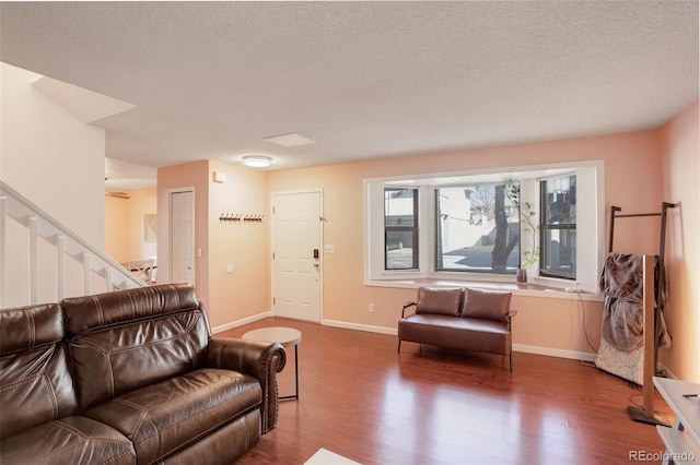 living area with a textured ceiling, stairs, baseboards, and wood finished floors