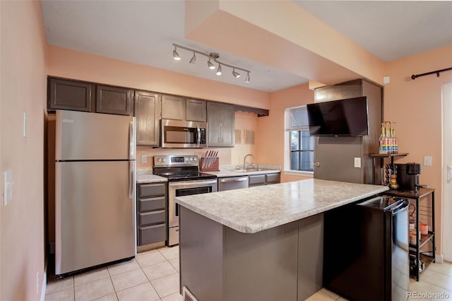 kitchen featuring a kitchen bar, a sink, appliances with stainless steel finishes, light tile patterned flooring, and light countertops