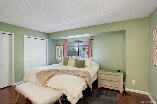 bedroom with wood finished floors, baseboards, two closets, and a textured ceiling