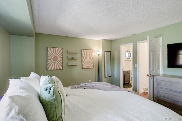 bedroom with connected bathroom, a textured ceiling, and visible vents