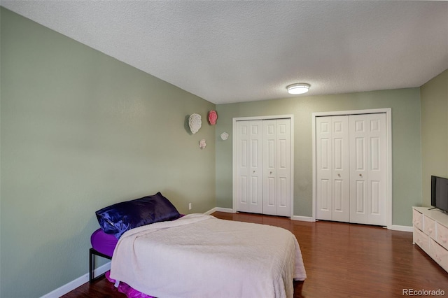 bedroom featuring baseboards, multiple closets, a textured ceiling, and wood finished floors