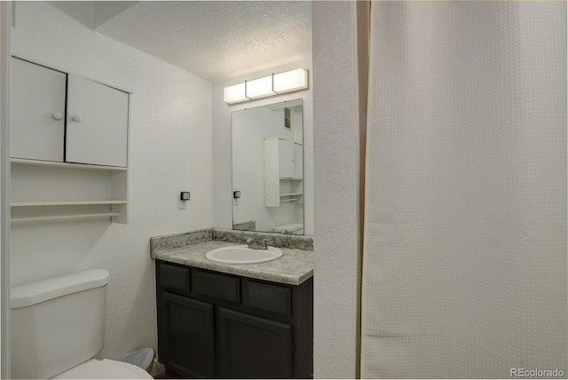 bathroom with vanity, toilet, a textured wall, and a textured ceiling