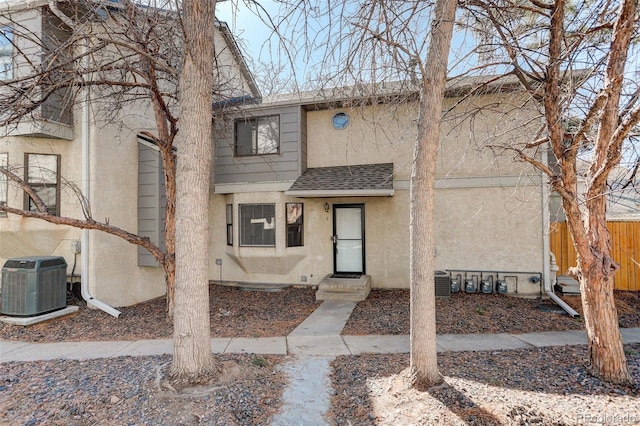 townhome / multi-family property featuring cooling unit, fence, roof with shingles, and stucco siding