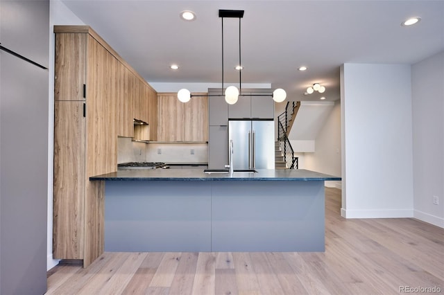 kitchen with kitchen peninsula, dark stone counters, high end refrigerator, light hardwood / wood-style flooring, and decorative light fixtures