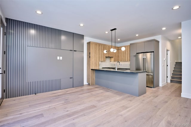 kitchen featuring kitchen peninsula, light hardwood / wood-style flooring, pendant lighting, high quality fridge, and sink