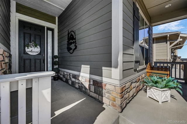 view of exterior entry featuring stone siding and covered porch