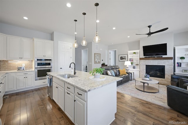 kitchen featuring light stone counters, dark wood-style flooring, a fireplace, appliances with stainless steel finishes, and a sink