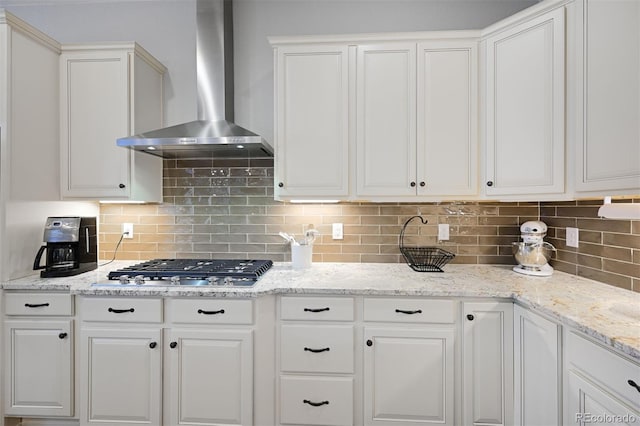 kitchen featuring tasteful backsplash, white cabinetry, stainless steel gas stovetop, and wall chimney range hood